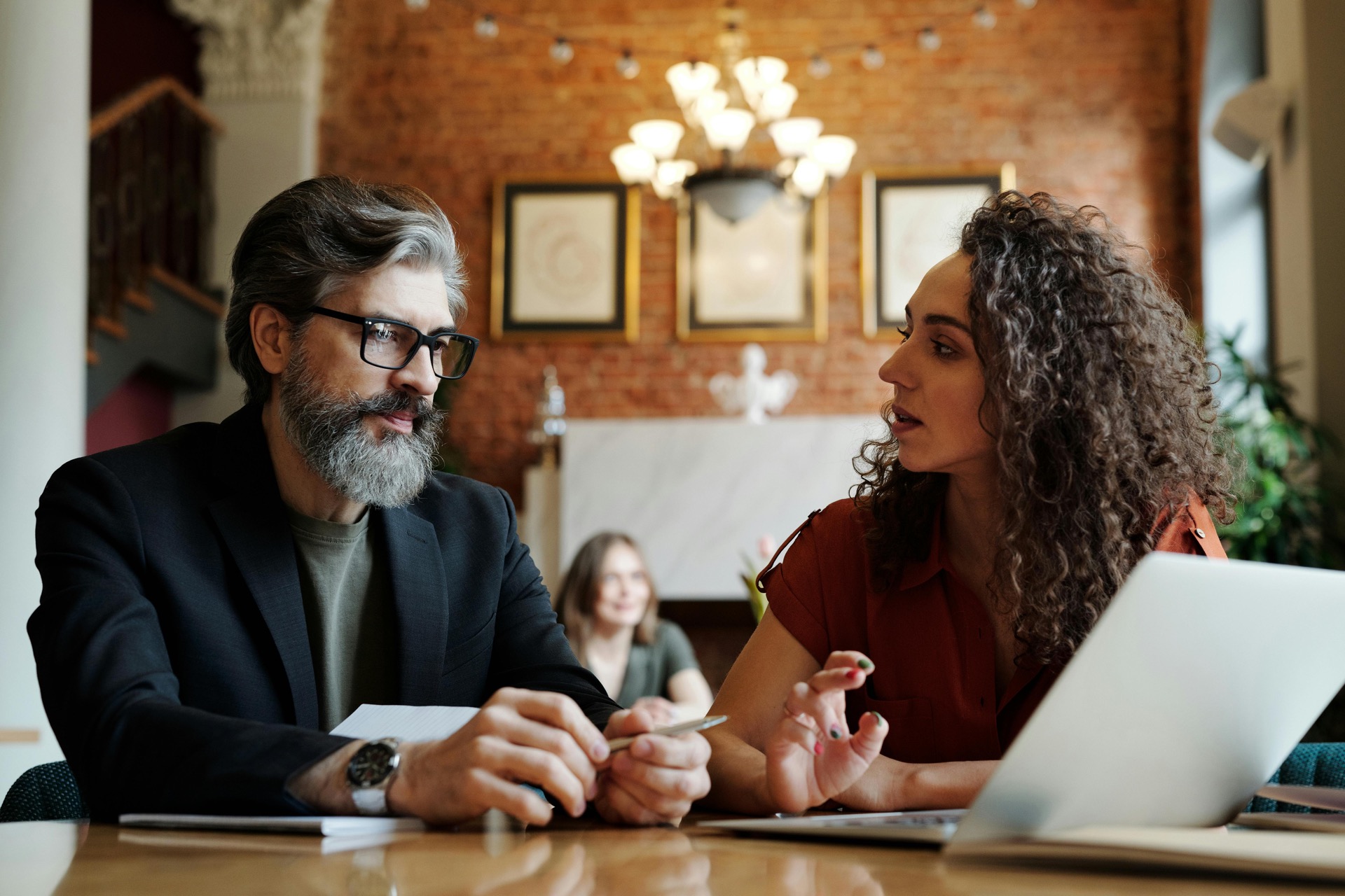 A founder in conversation with a colleague at a desk in a brick-walled office