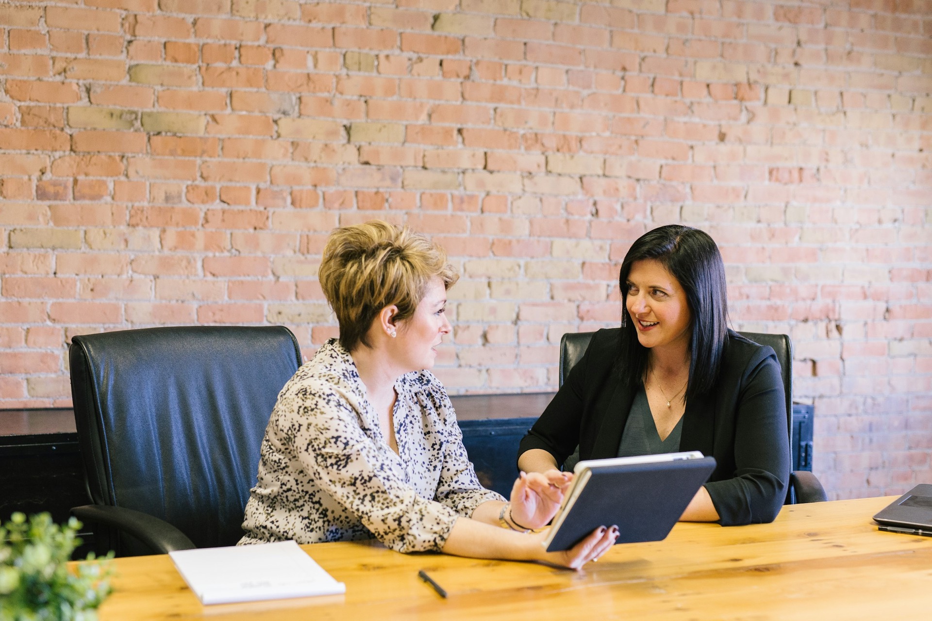 Two women in coaching conversation at a desk in front of a brick wall